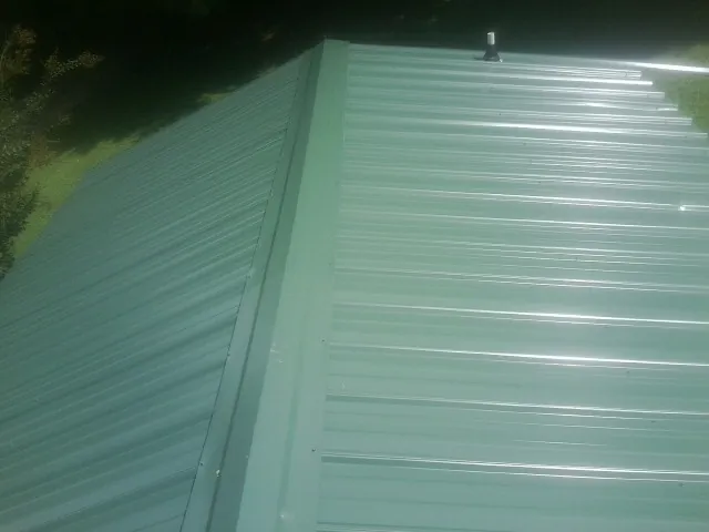 New green metal panels meeting at the ridge of a roof — Flat Roof Repair work by our crew in Matlock