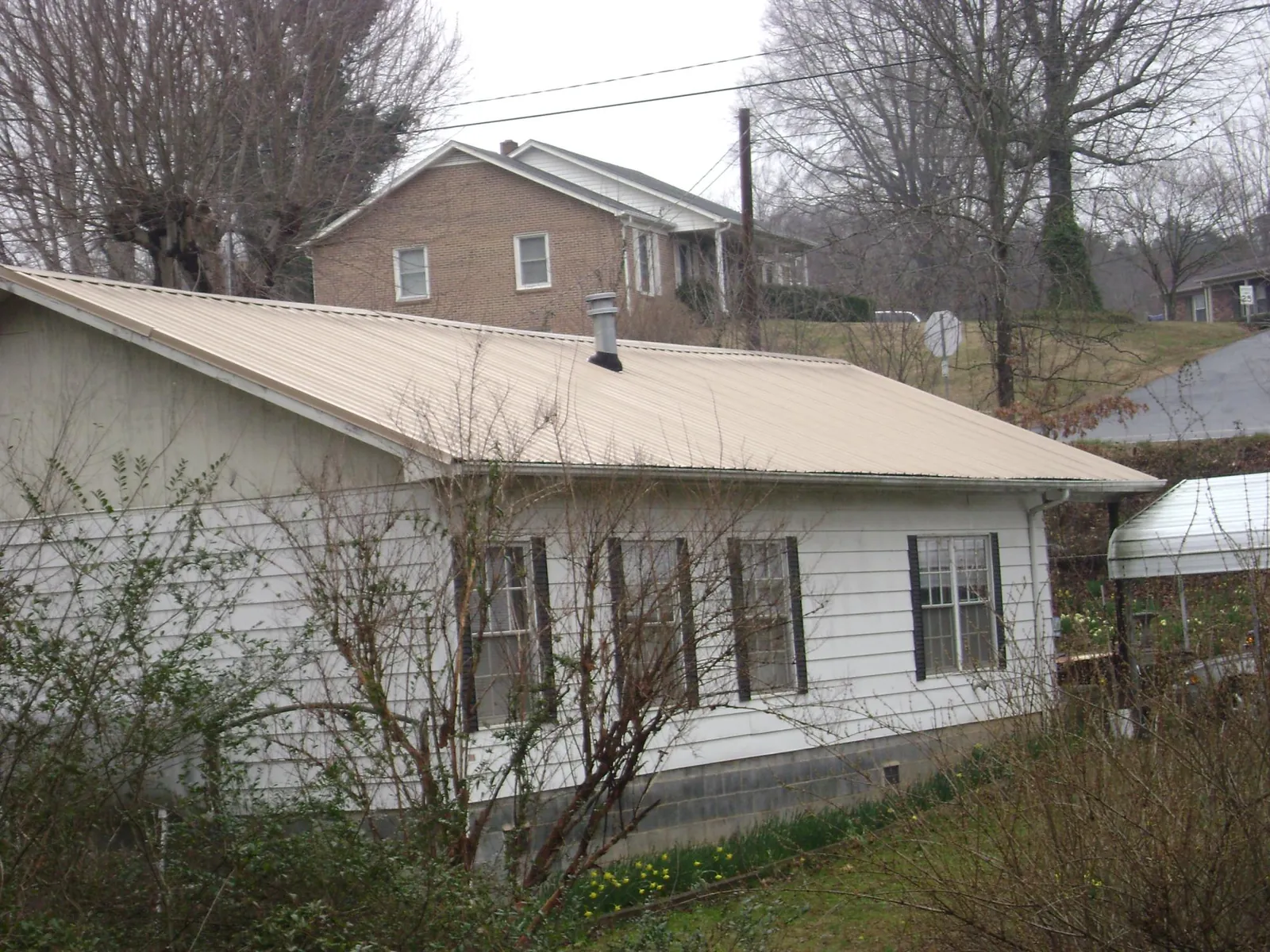 Tan metal roof on a white sided house set into a hillside — Commercial Roofing by Roofing Brothers in Matlock